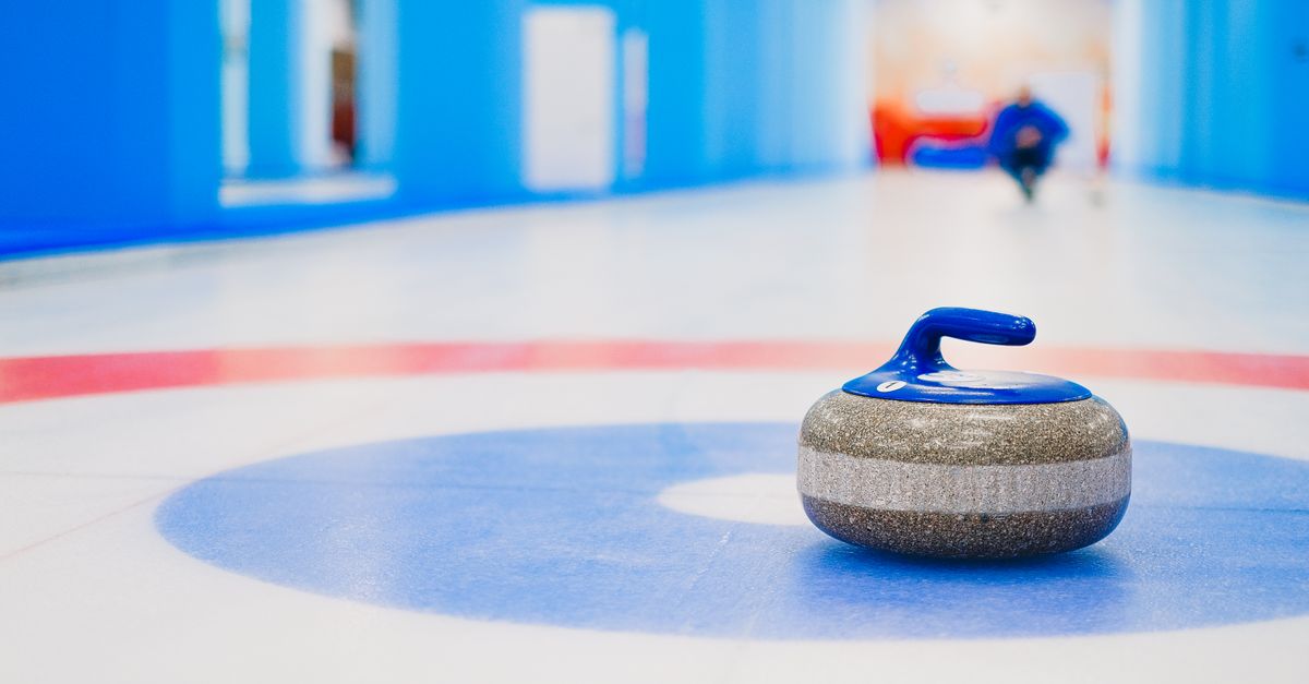 Curling gray stone with blue handle placed on blue circle on modern ice rink